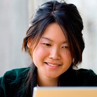 Photograph of a woman reading from a laptop monitor.