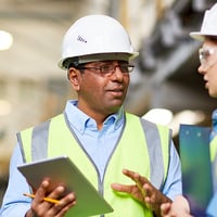 A man and woman wearing hardhats and carrying a tablet