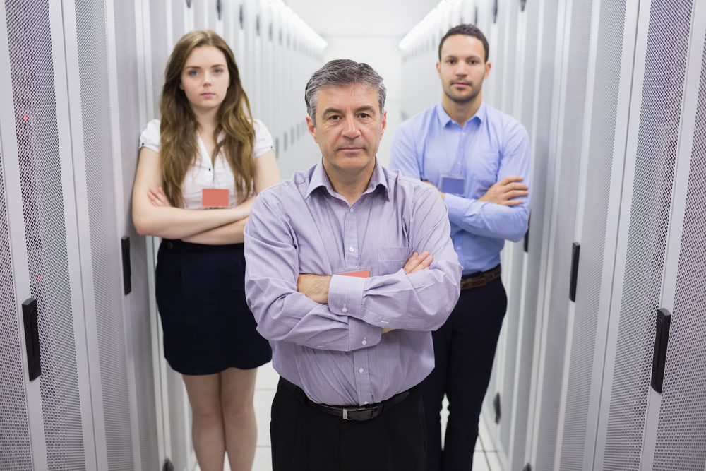 Three people standing in data center with arms crossed looking serious